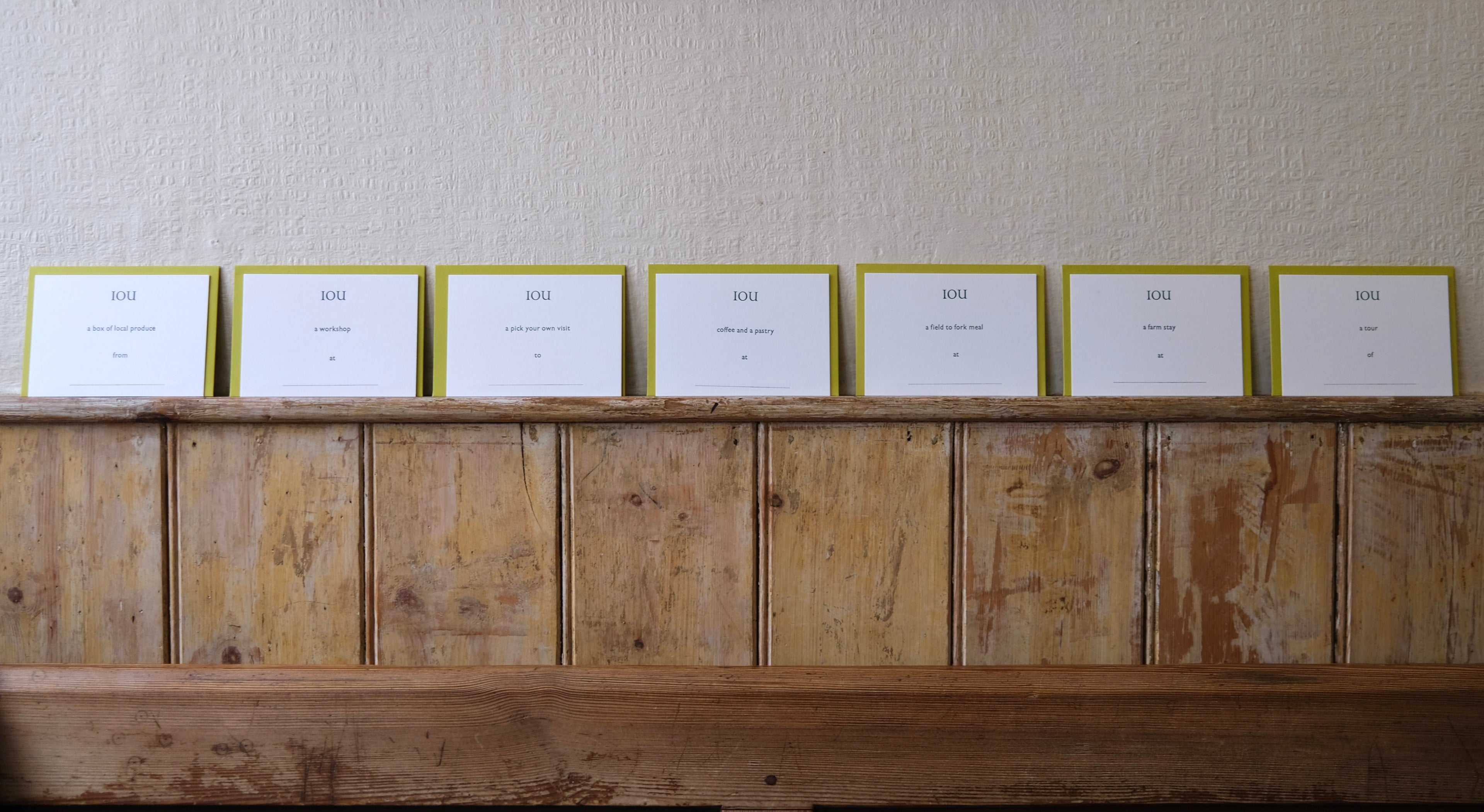 Row of IOU gift cards on a wooden shelf against a textured wall.